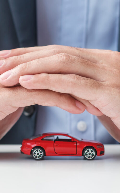 Businessman hand cover or protection red car toy on table. Car insurance, warranty, repair, Financial, banking and money concept